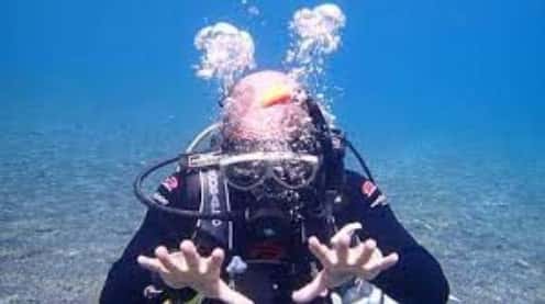 ダイビング水中スキルのレギュレータクリアで勢いよくレギュレータの中に息を拭くダイバー