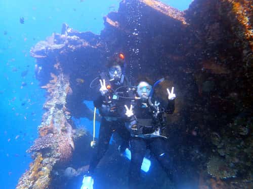 バリ島トランベンの沈船をバックに水中で記念撮影するカップルダイバー