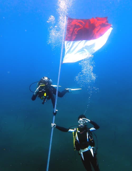 インドネシア独立記念日に水中に設置されたインドネシア国旗と共に敬礼しこの日を祝う2人のダイバー