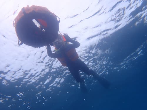 水面に浮かぶフロートに掴まったライフジャケットを着たシュノーケラーを下から見上げた海景