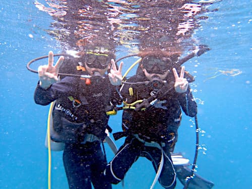 水面下でピースサインをする2人の少年ダイバーの海景