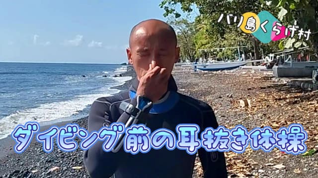 ダイビング前にバリ島トランベンのビーチで耳抜き体操する坊主頭のダイビングインストラクター