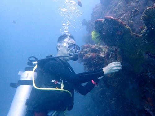 トランベンの沈船の配管のハンドルと記念撮影するダイバー