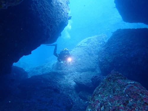 バリ島くらげ村のヌサペニダの地形ダイビングで大きな岩の下を潜るベテランダイバー