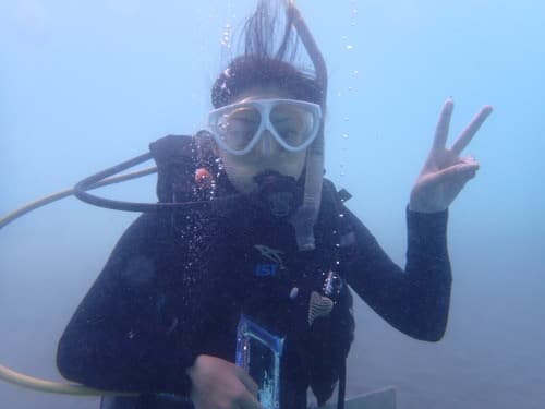 ちょっと濁ってる海中でピースサインをする女性ダイバー