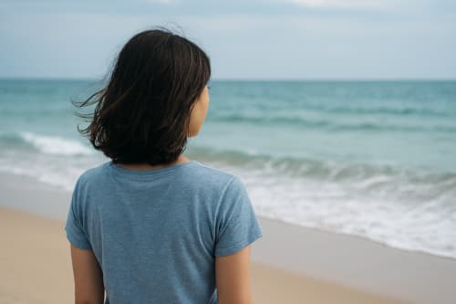 海を見ながら不安を感じまがらビーチに佇む女性の後ろ姿