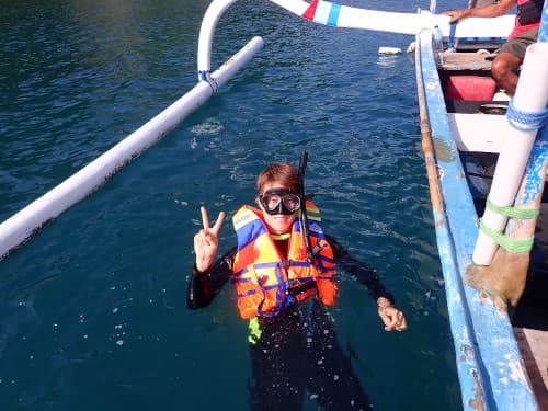 バリ島パダンバイのシュノーケリングでジュクンから水面に押してピースしている男性シュノーケラー