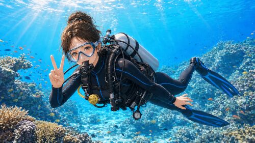 バリ島のサンゴ礁でカメラに向かってピースサインをする女性ダイバー