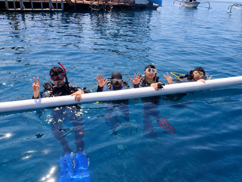 バリ島の体験ダイビングで海面に浮かびながら記念撮影する大学時代の友人3人とガイド